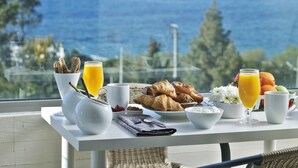 A breakfast table with croissants, fruit, and orange juice on a balcony overlooking the sea. - Amarilia Hotel (Vari-Voula-Vouliagmeni)