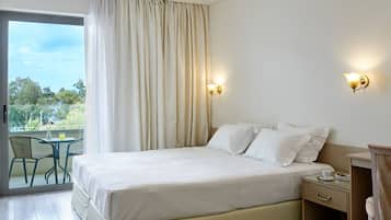 A hotel room with a bed, a nightstand, a chair, and a table with a drink.