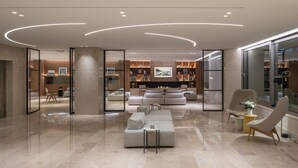 A modern living room with a sectional sofa, a coffee table, and a fireplace. There is a glass partition with a wooden frame, and a large window on the right side. - Amarilia Hotel (Vari-Voula-Vouliagmeni)