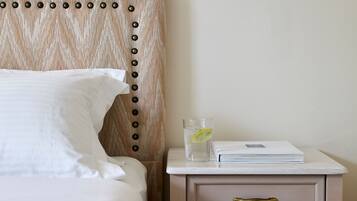 A neatly made bed with white linens, a bedside table with a glass of water and a book, and a drawer with a brass handle.