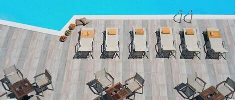A poolside area with lounge chairs and tables, a pool, and umbrellas.