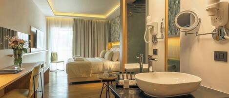 A hotel room with a large bed, a desk with a chair, a round mirror, a sink, and a hairdryer.