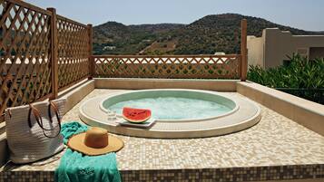 Un jacuzzi con vistas a colinas, un bolso tejido, un sombrero de paja y una toalla verde.