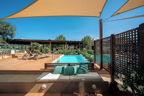 A pool area with sun loungers, a pool, and a covered seating area.