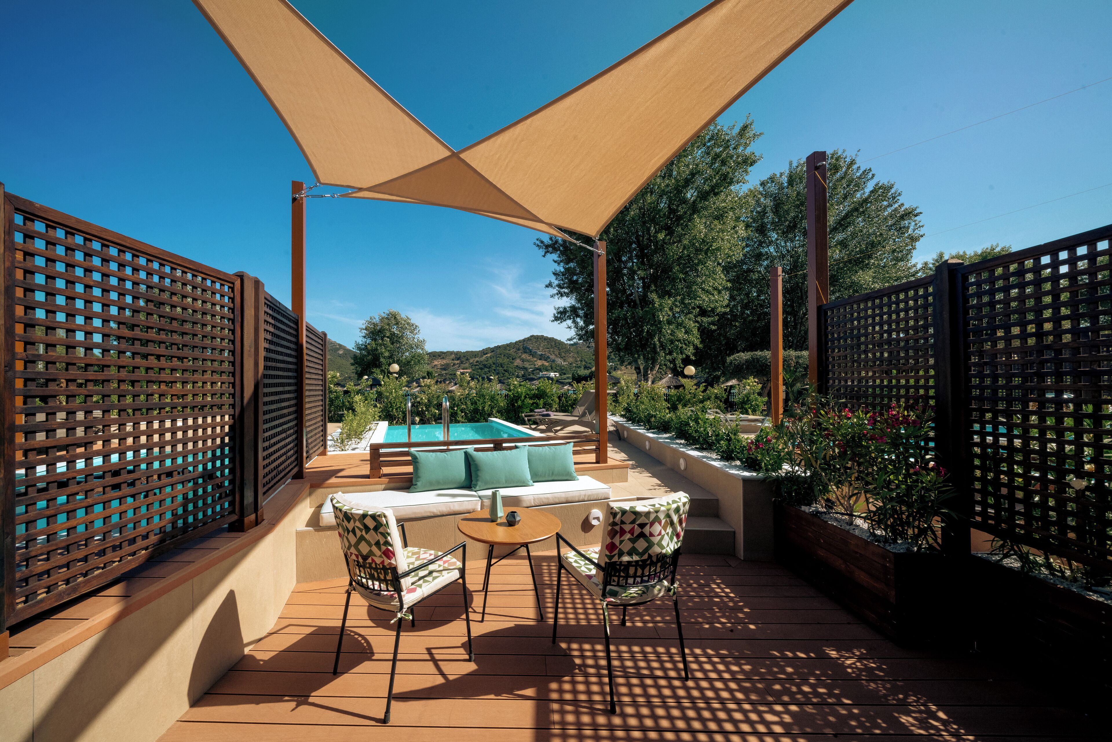 Une terrasse extérieure ensoleillée avec une piscine, un espace salon et des clôtures en bois.