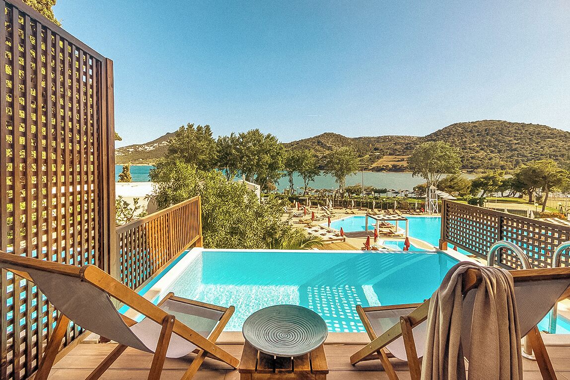 Ein Poolbereich mit Liegestühlen und Blick auf einen See und Hügel.