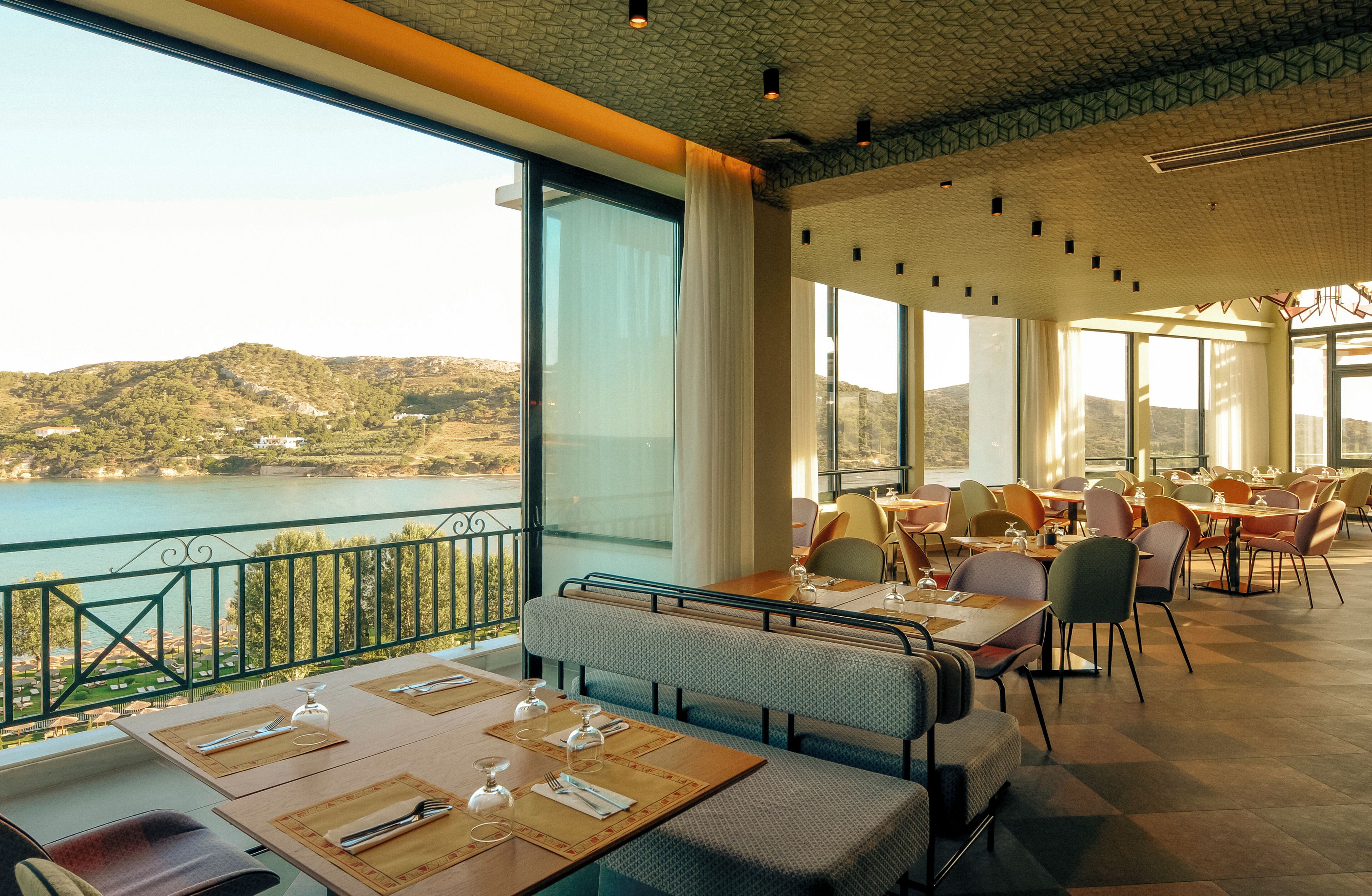 A restaurant with outdoor seating overlooking a lake, featuring large windows and a view of the landscape.