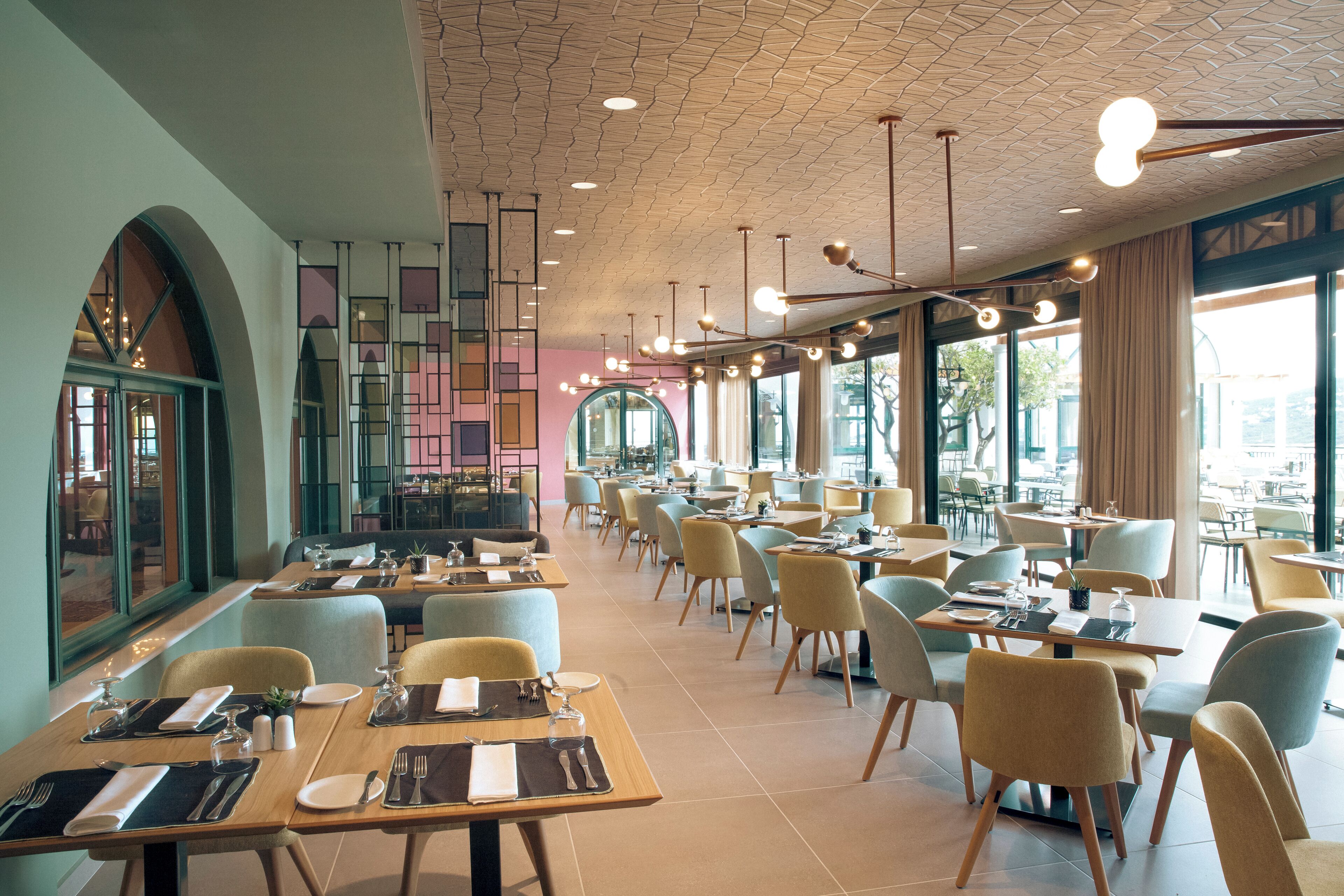 Un restaurante moderno con varias mesas y sillas, ventanas amplias y un techo con diseño.