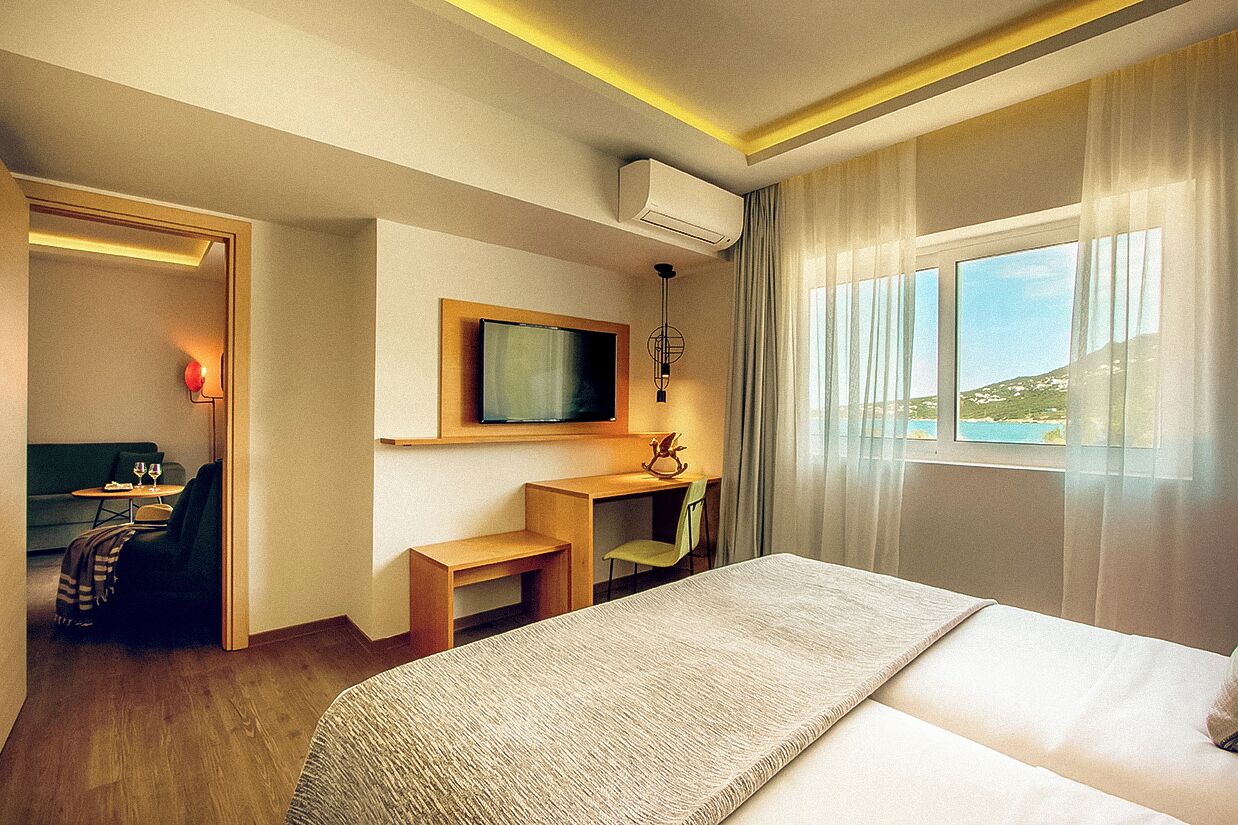 Habitación de hotel con una cama grande, un escritorio, una silla, un televisor y una ventana con vistas al exterior.