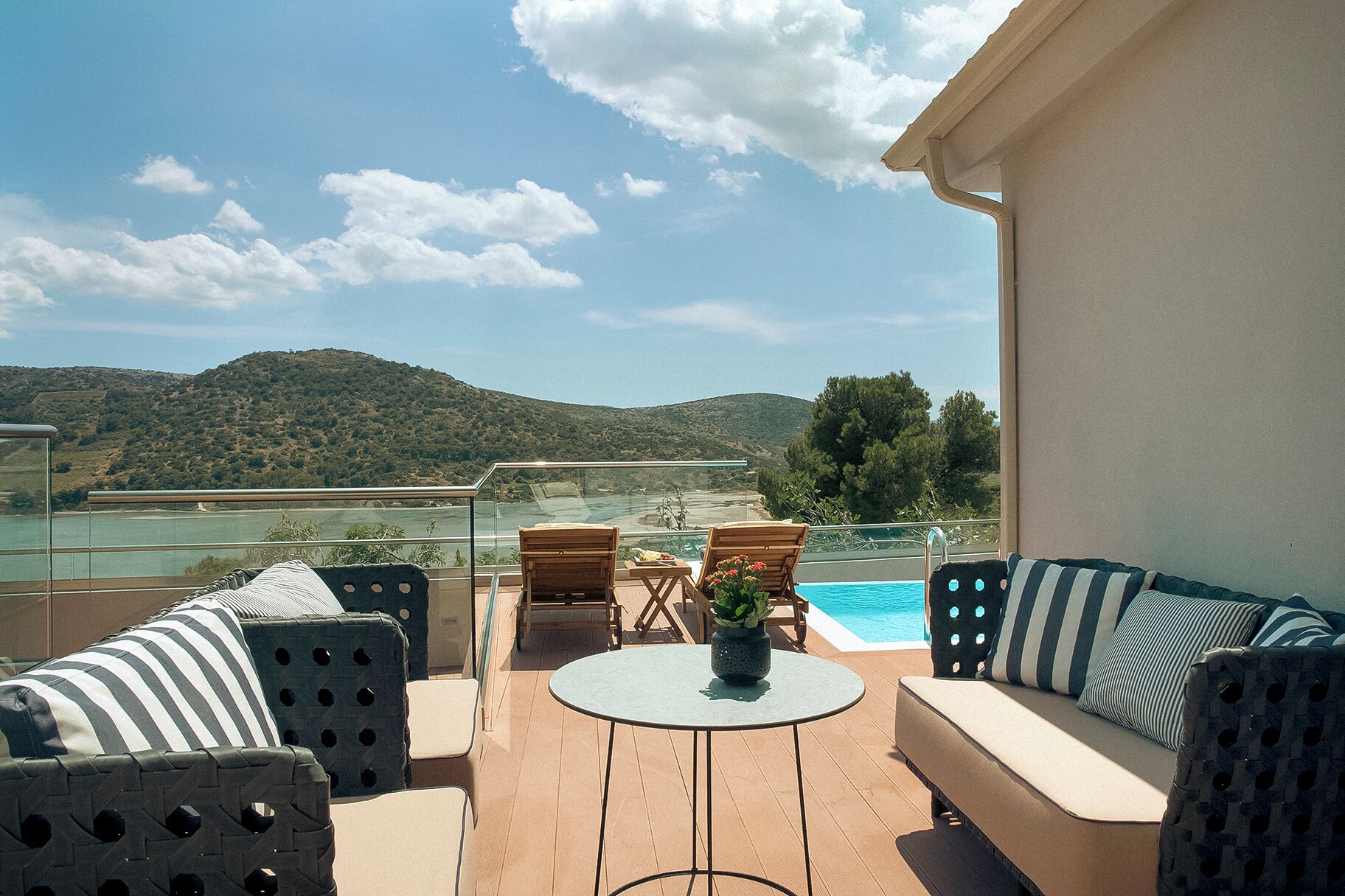 A terrace with a pool, wooden furniture, and a view of hills.