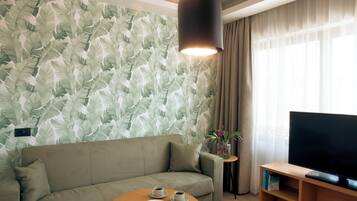 A modern living room with a sofa, a coffee table with cups and pastries, a flat-screen TV, and a wall with a leafy pattern.