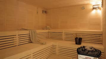 A sauna with wooden benches, a bucket, and a bag of charcoal.