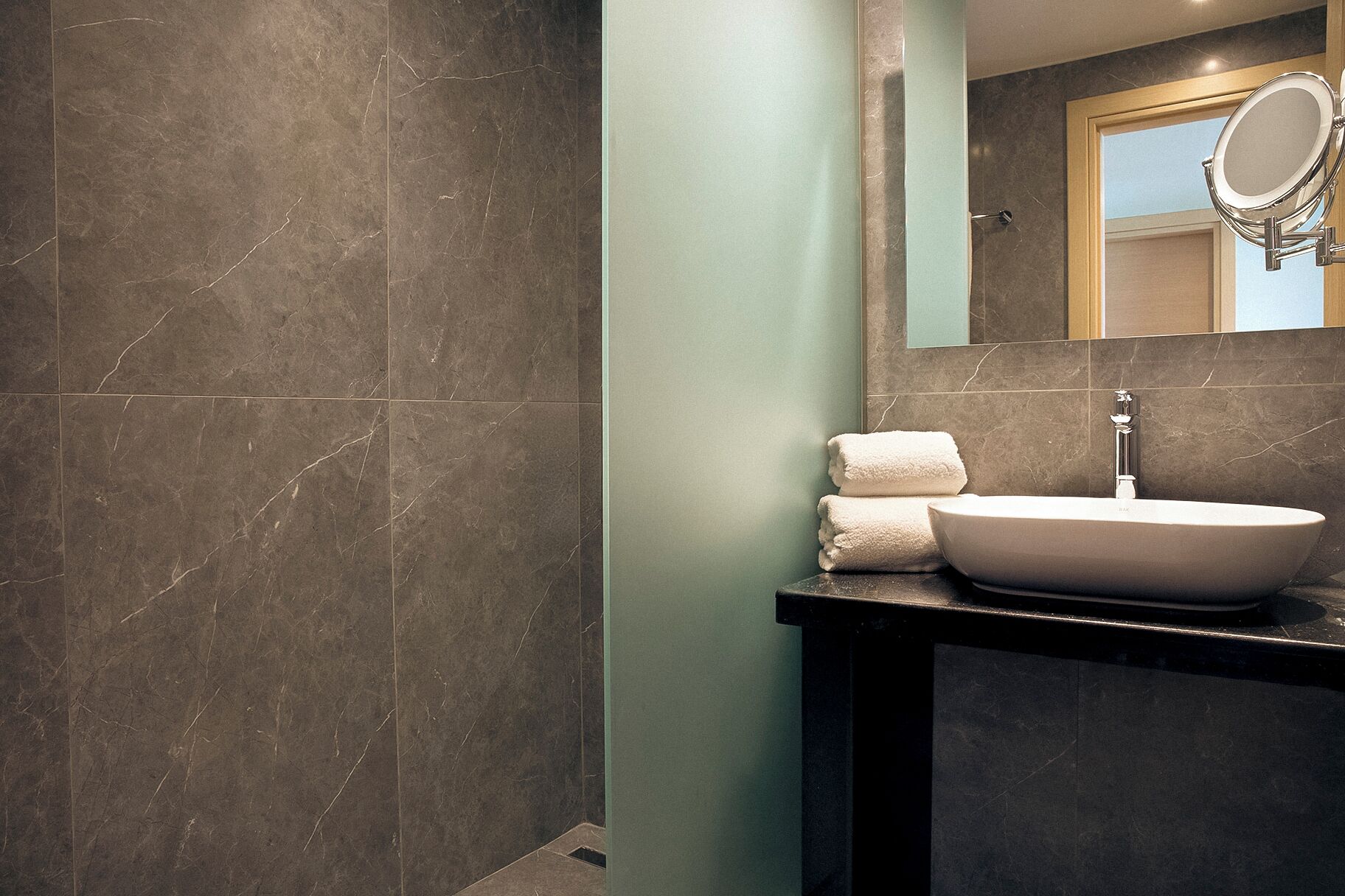 Un baño con baldosas de mármol oscuro, un lavabo blanco, un espejo y una toalla.