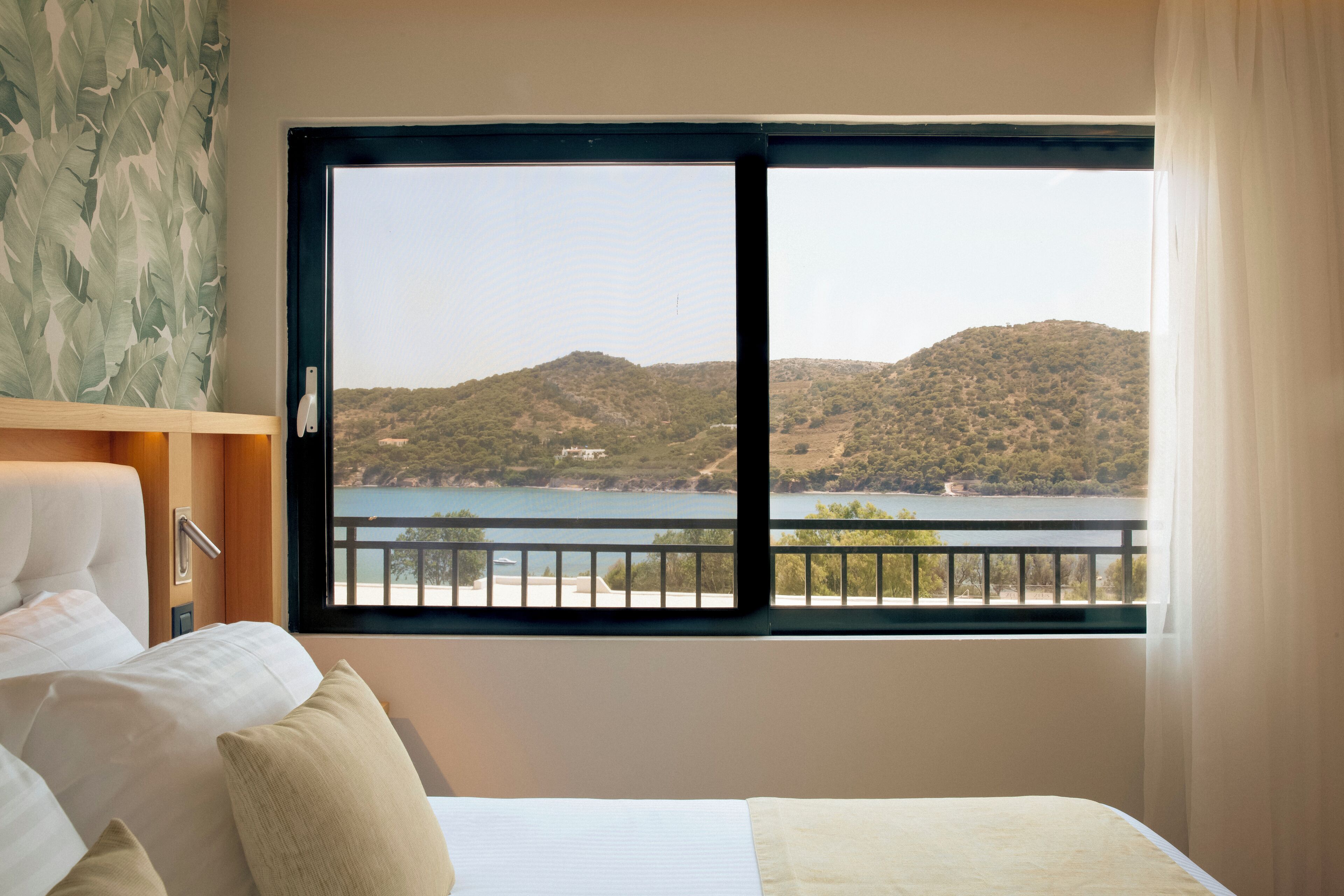 Une chambre d’hôtel avec un lit, une table de chevet et une fenêtre donnant sur un lac et des collines.