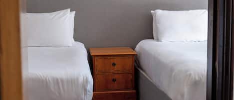 A small, neatly arranged bedroom with two single beds, a wooden nightstand, and a grey wall.