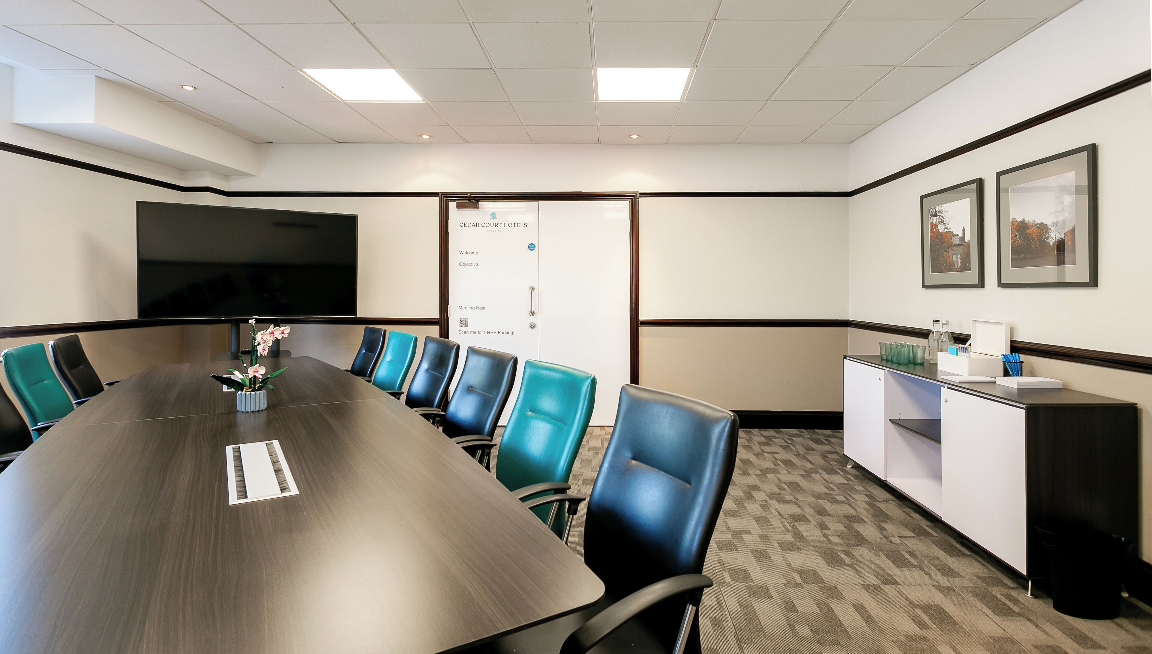 A conference room with a long table, blue chairs, a whiteboard, and a reception desk with a coffee machine.