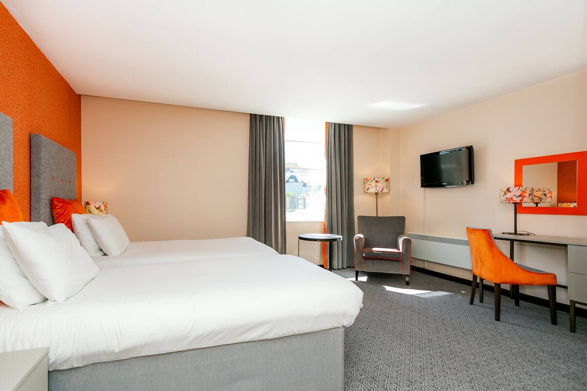 A hotel room with a large bed, a desk, a chair, a television, and a window with curtains.