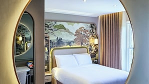 A hotel room with a large round mirror, a bed with white linens, a nightstand, a lamp, and a mural on the wall. - Cedar Court Harrogate (Harrogate)