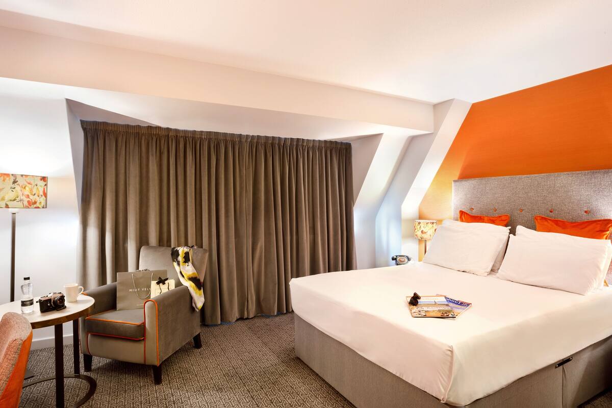 A hotel room with a bed, a chair, a table, and a large window with curtains.