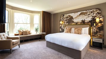 A spacious bedroom with a large bed, a seating area by the window, and a decorative headboard.