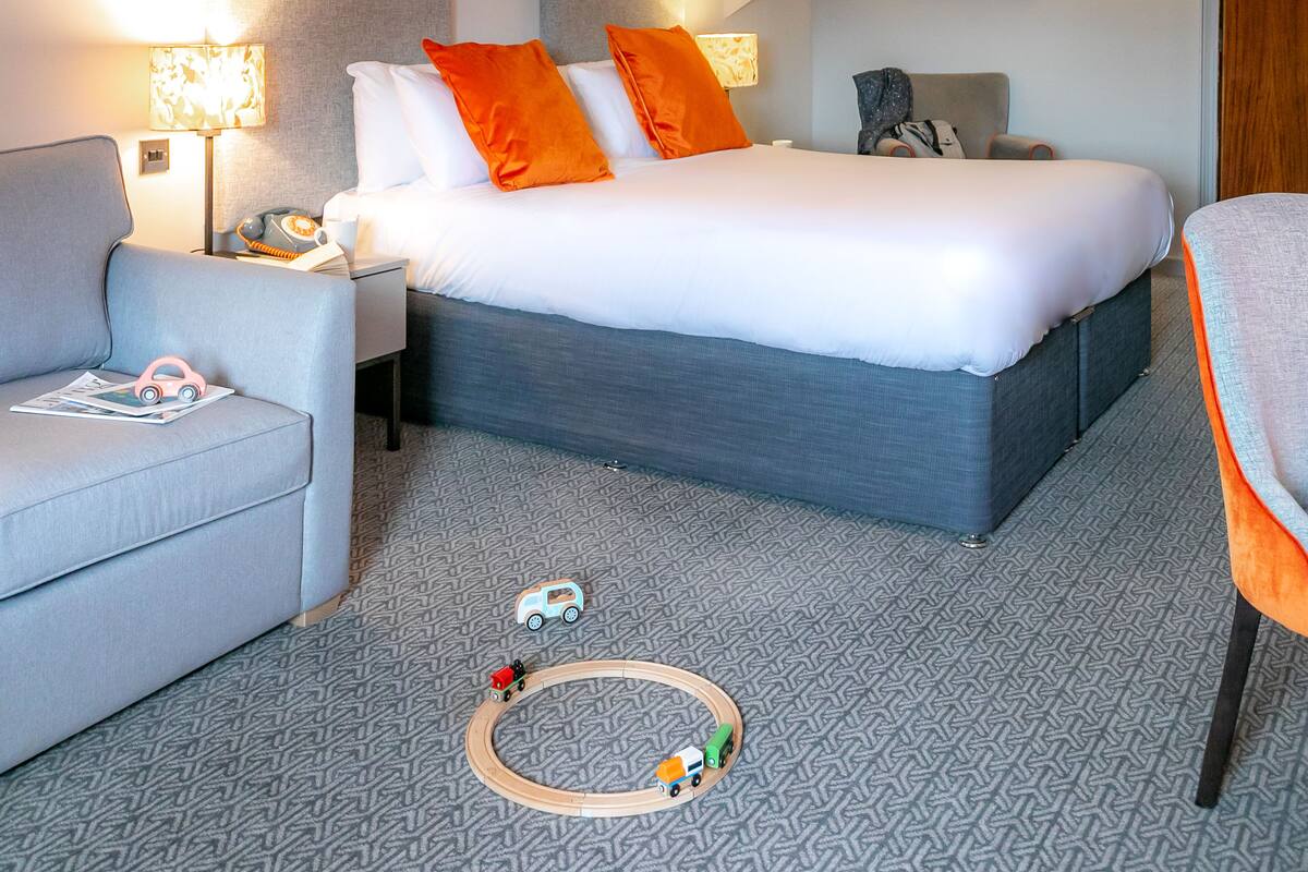 A hotel room with a bed, a sofa, a desk, and a toy train set.