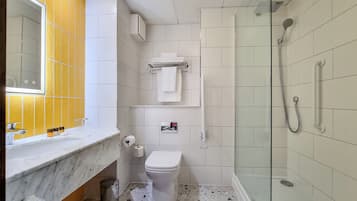 A modern bathroom with a marble countertop, a toilet, a glass-enclosed shower, and a mirror with a yellow accent wall.