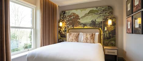 A neatly made bed with a headboard featuring a landscape mural, a bedside table with a lamp, and a window with curtains.