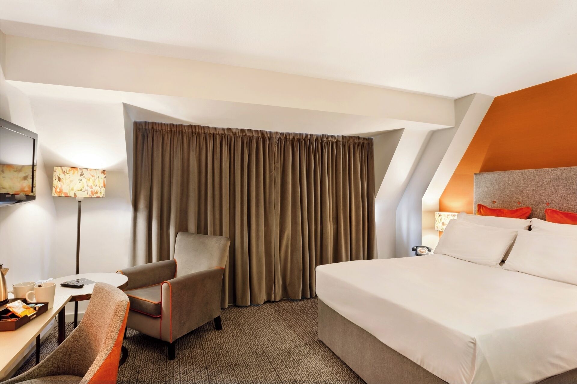 A hotel room with a bed, a desk, a chair, a TV, and a window with curtains.
