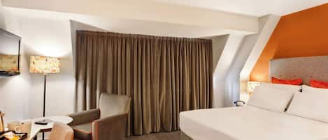 A hotel room with a bed, a desk, a chair, a TV, and a window with curtains.