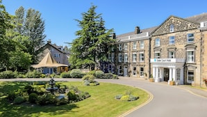 A hotel with a traditional stone facade, a well-maintained garden with a fountain, and a clear blue sky. - Cedar Court Harrogate (Harrogate)