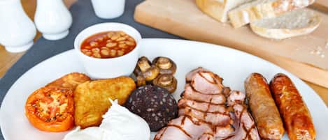 A plate of food including sliced ham, sausages, beans, mushrooms, and a boiled egg.