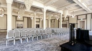A conference room with rows of chairs, a stage with a podium, and ornate chandeliers. - Cedar Court Harrogate (Harrogate)