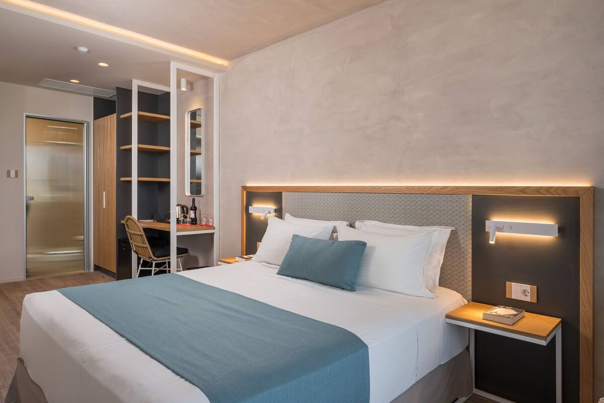 A modern hotel room with a large bed, bedside tables, a desk, and a wardrobe.