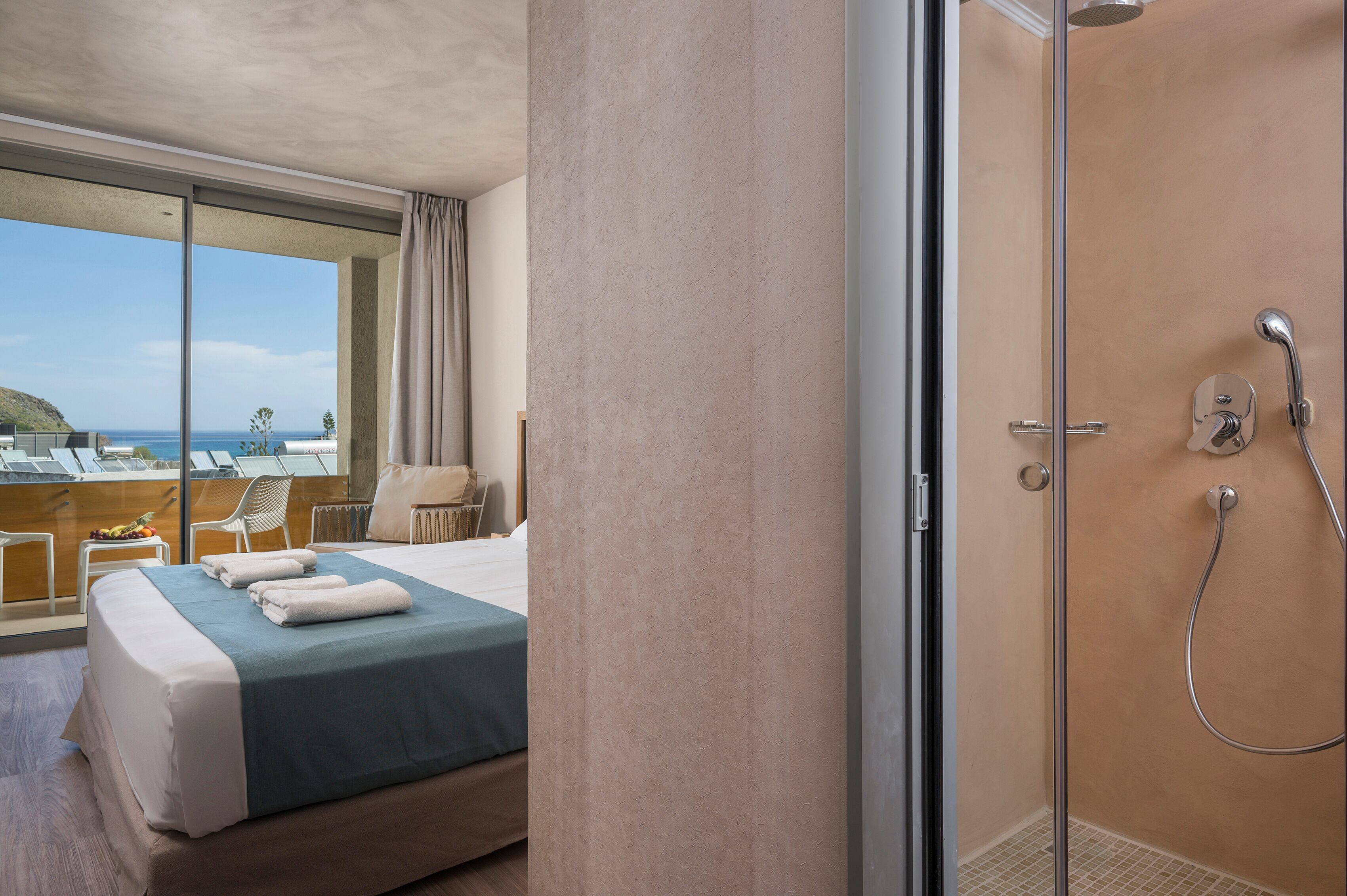 A hotel room with a large bed, a shower, and a balcony with a view of the ocean.