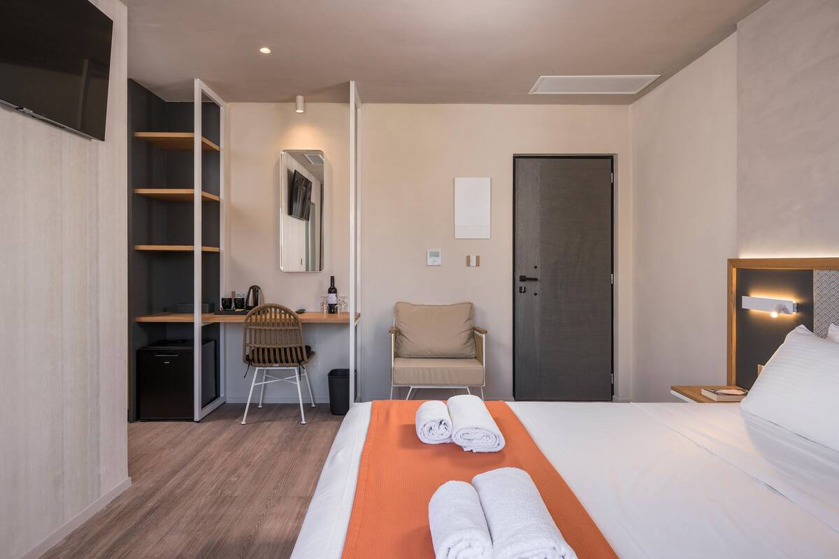 A hotel room with a bed, a desk, a chair, a wardrobe, and a TV.