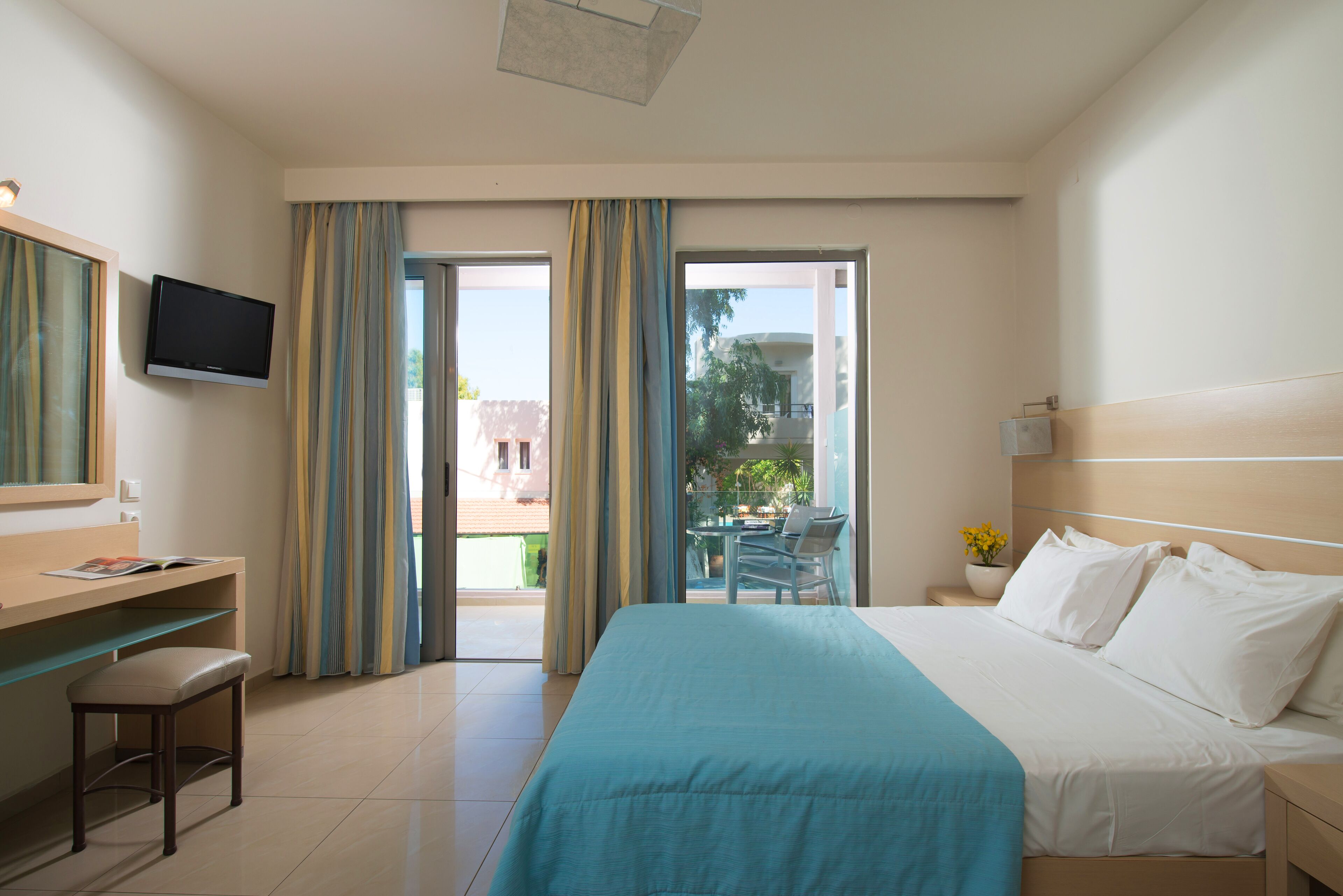 A hotel room with a bed, a desk, a chair, a TV, and a balcony with curtains.