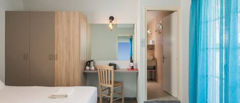 Una habitación de hotel con cama, escritorio con silla, espejo y ventana con cortinas azules.