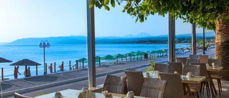 A seaside restaurant with outdoor seating, tables, and chairs, overlooking the ocean.