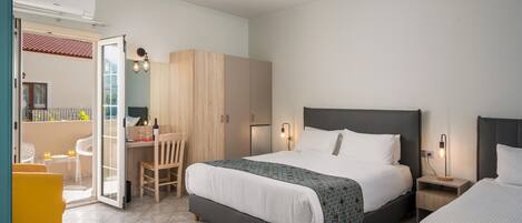 A modern hotel room with a large bed, a desk, and a chair. There is a wardrobe, a nightstand, and a small table with a lamp.