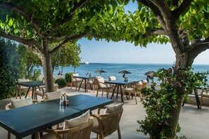 An outdoor seating area with tables and chairs, overlooking a body of water. - Corissia Beach Hotel (Apokoronas)