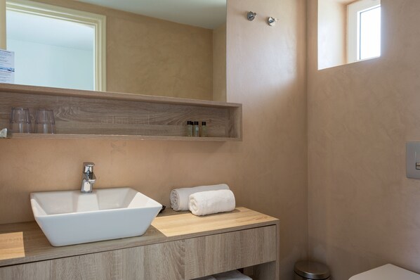 A bathroom with a rectangular sink, a wooden vanity, a towel, and a mirror above the sink. - Corissia Beach Hotel (Apokoronas)