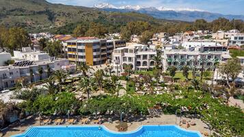 Un resort con piscina, palmeras y montañas al fondo.