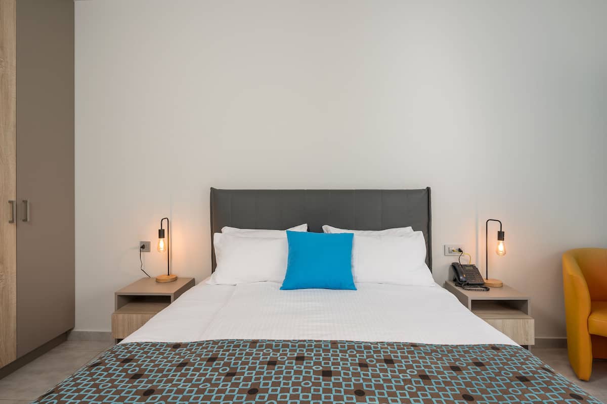A neatly made bed with a blue pillow, two bedside tables with lamps, and a yellow chair.