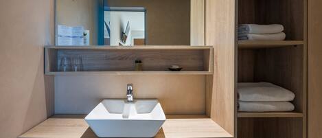 A modern bathroom with a white sink, wooden shelves, and a mirror.