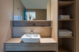 Un baño moderno con un lavabo blanco, estantes de madera y un espejo.