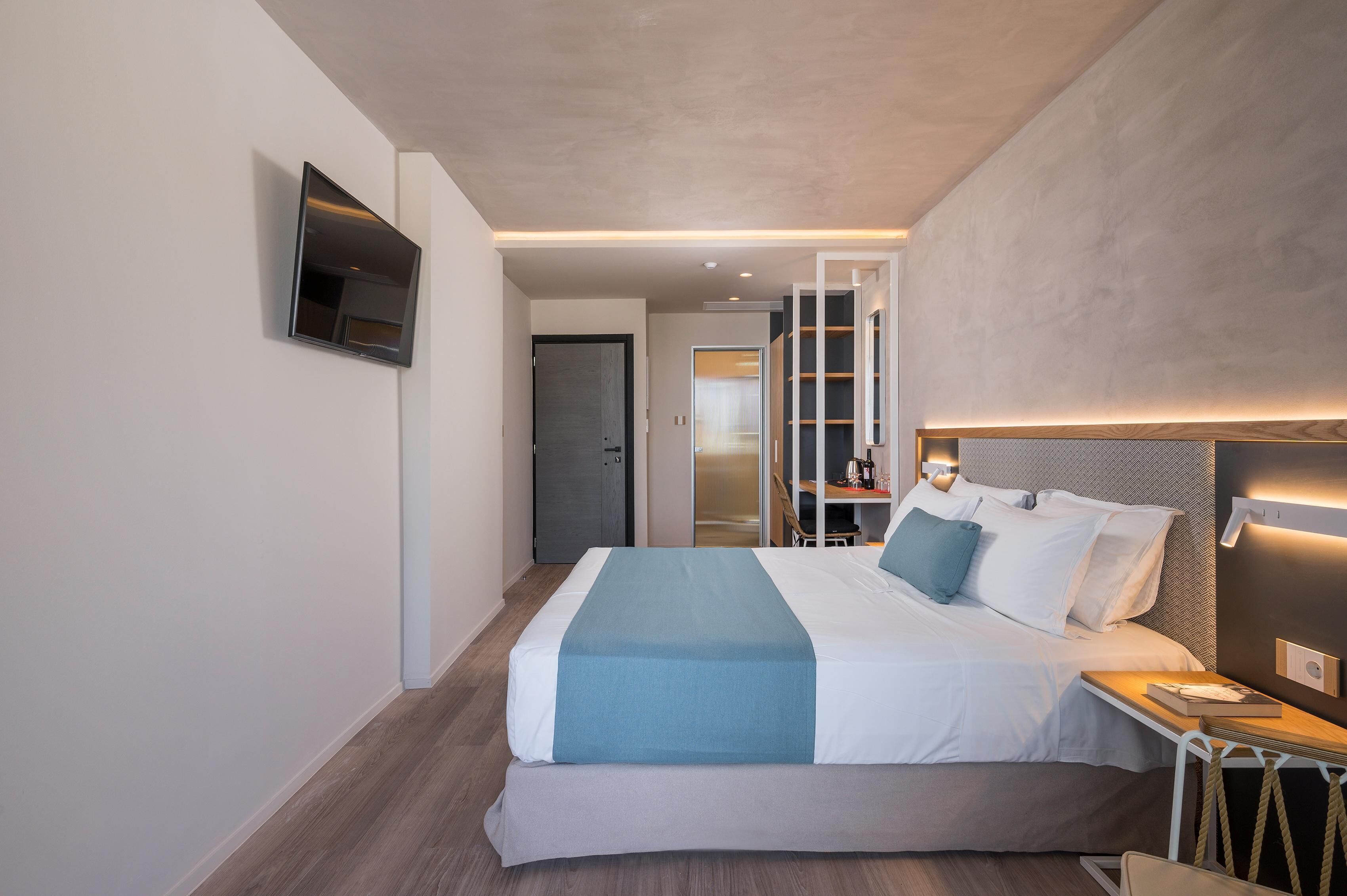Una moderna camera d'albergo con un grande letto, una televisione a schermo piatto montata a parete, un comodino con una lampada e vista sul corridoio.