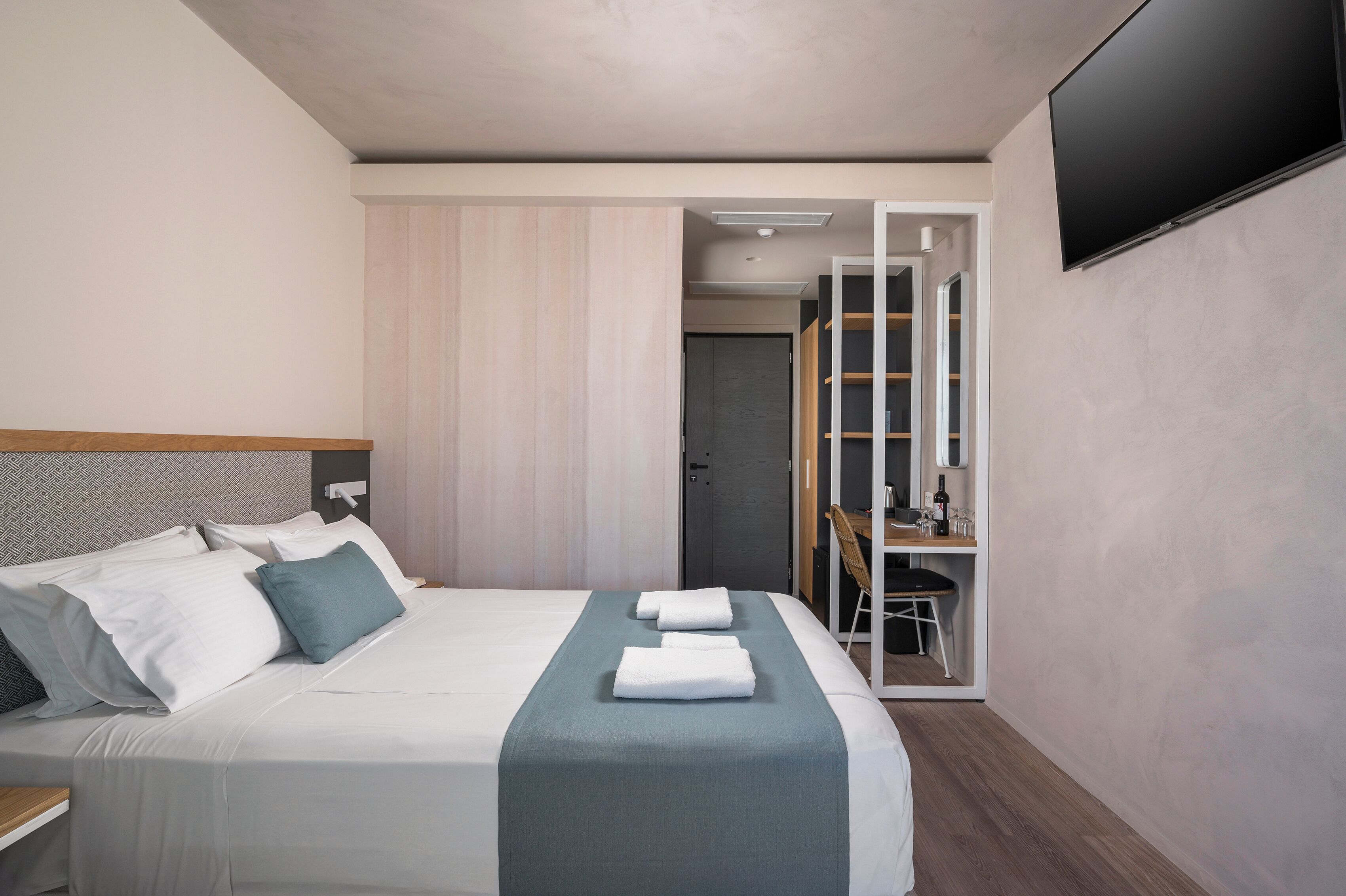 Une chambre d’hôtel moderne avec un grand lit, un bureau et un téléviseur fixé au mur.