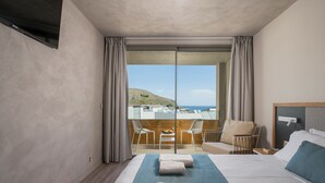 Een hotelkamer met een groot bed, een balkon met uitzicht op zee en een tafel met stoelen.