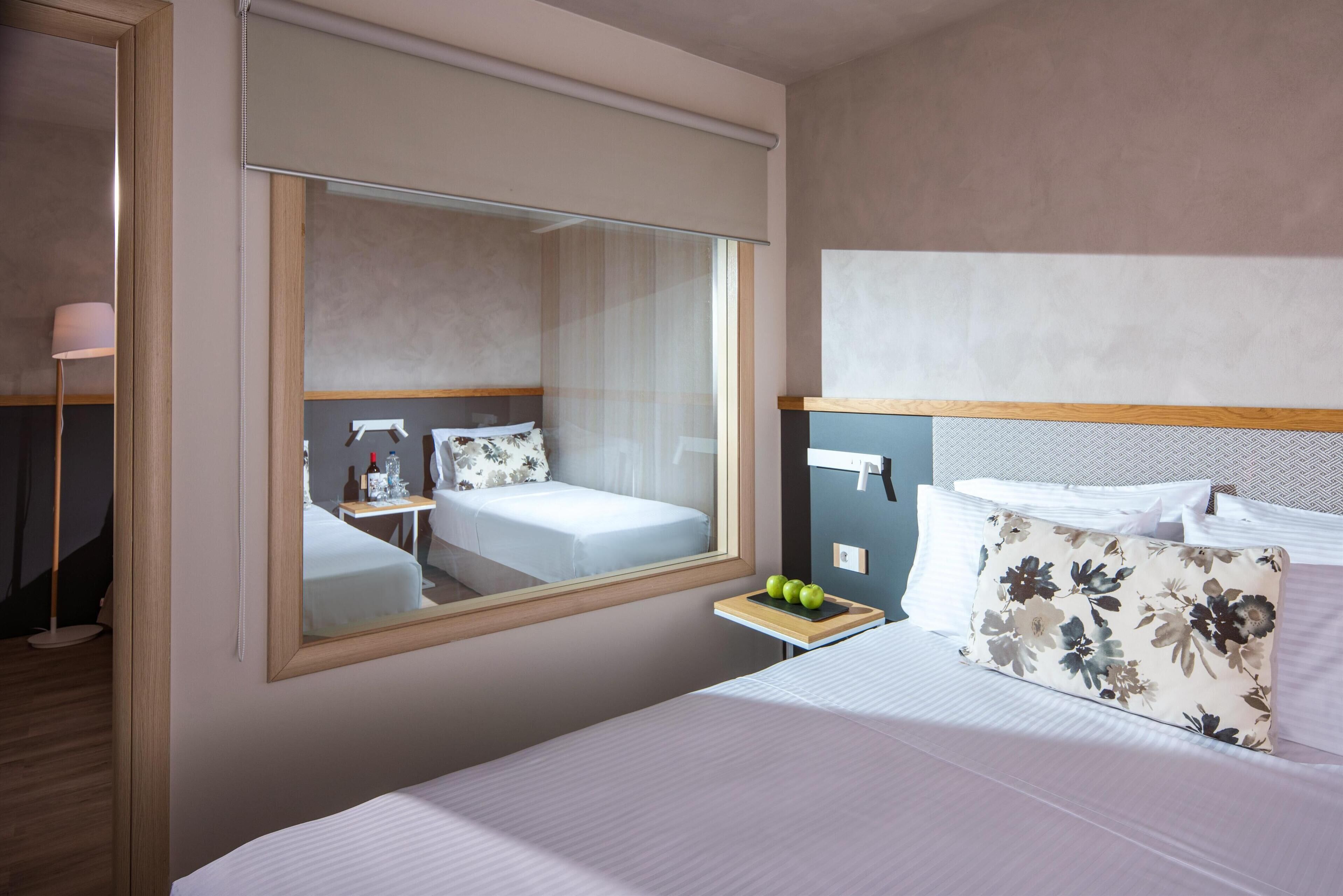 Una habitación de hotel con un espejo grande, una cama con ropa de cama blanca, una mesita de noche con una manzana verde y una almohada estampada con motivos florales.