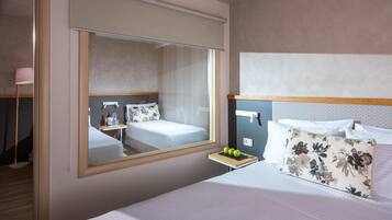 Una habitación de hotel con un espejo grande, una cama con ropa de cama blanca, una mesita de noche con una manzana verde y una almohada estampada con motivos florales.